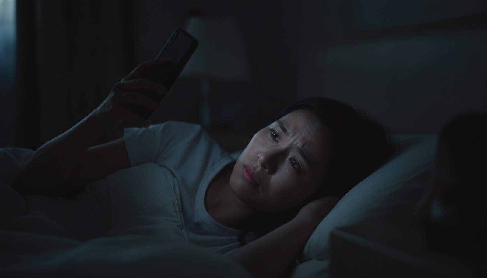 深夜卧室妈妈躺黑暗中举手机搜索脸被屏幕光照亮焦虑
